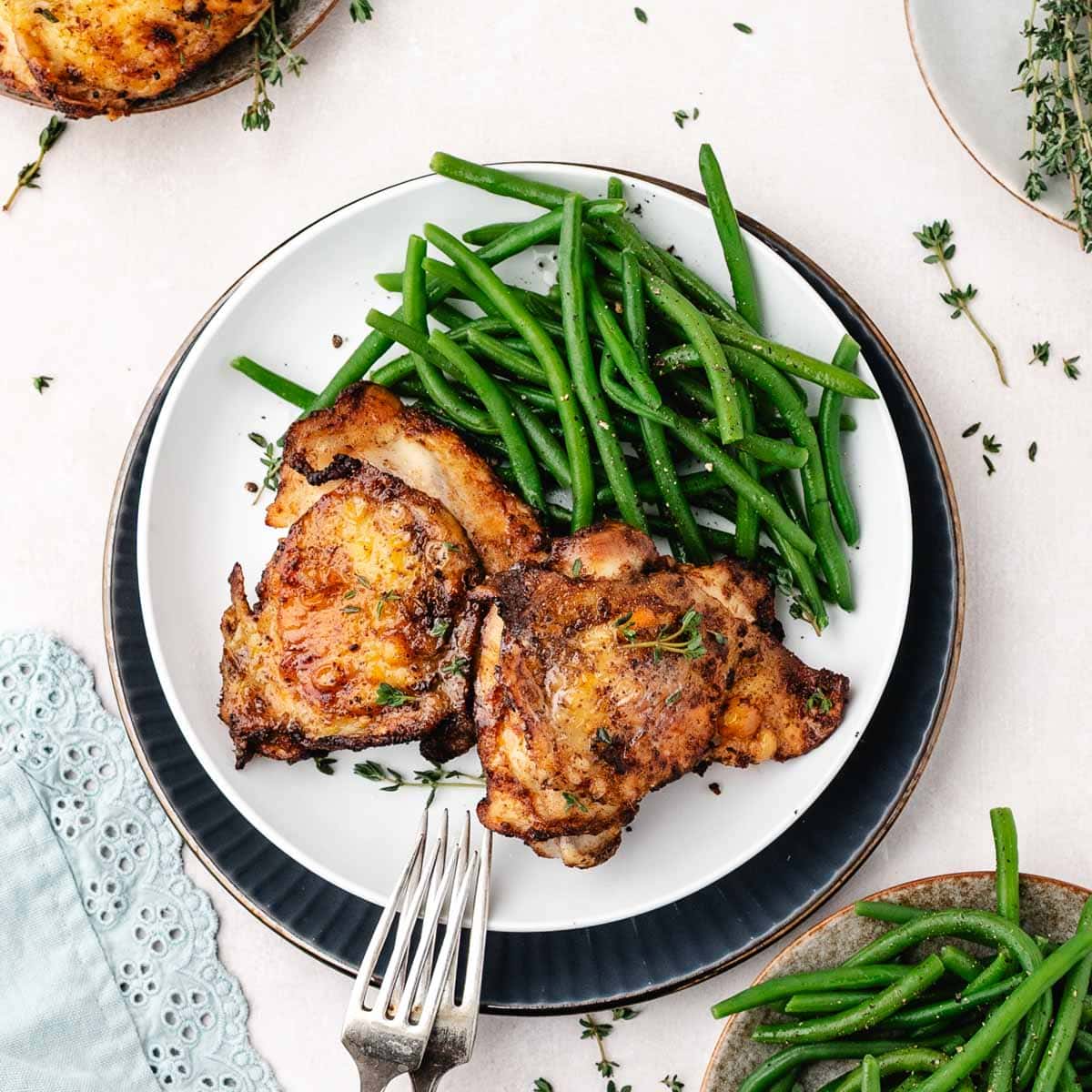 Two baked chicken thighs served with green beans on a plate.