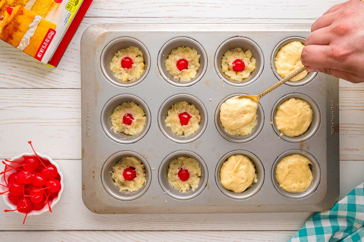 Spooning pineapple cake batter into the muffin tins.