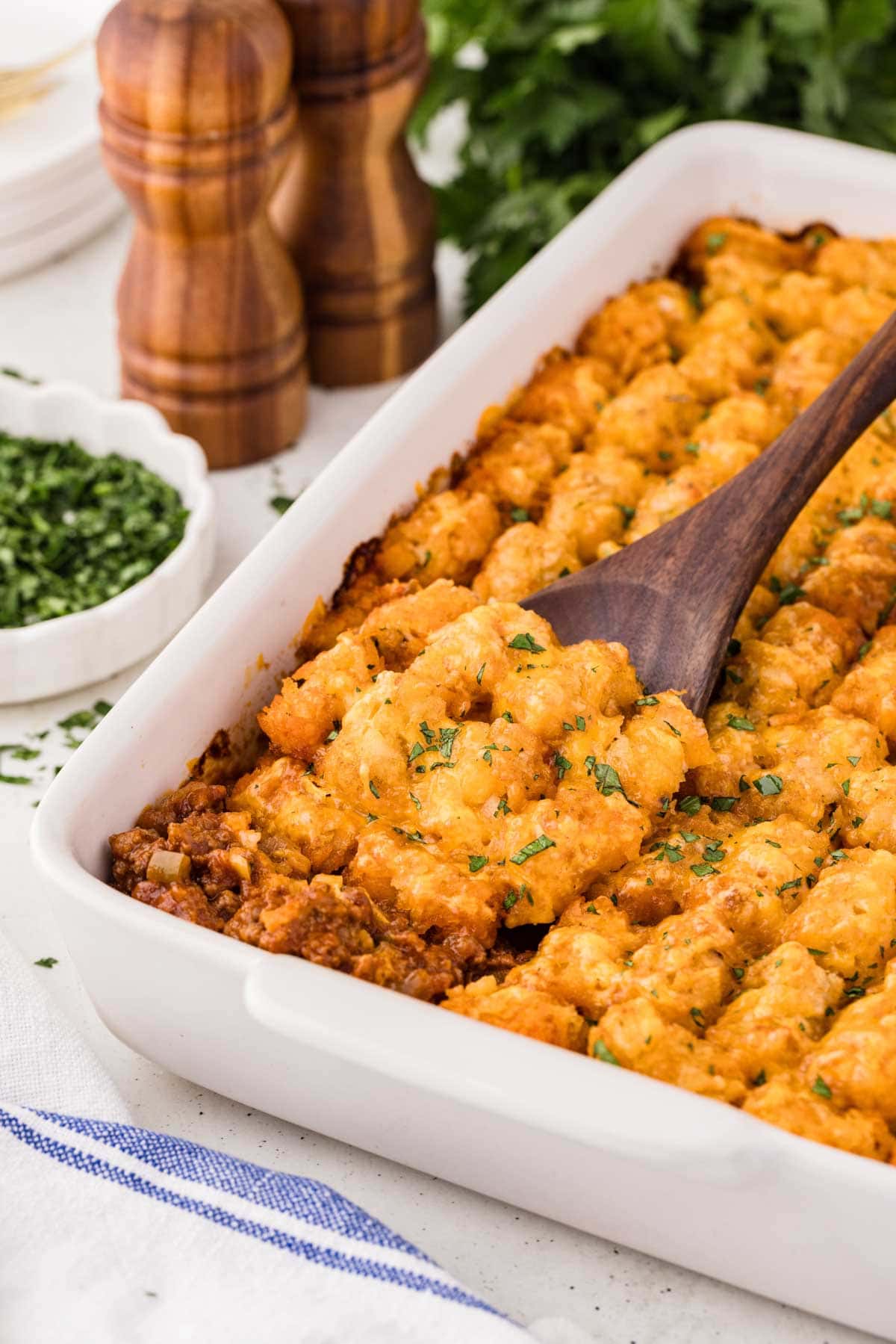 Wooden spoon scooping up a portion of sloppy joe tater tot casserole.