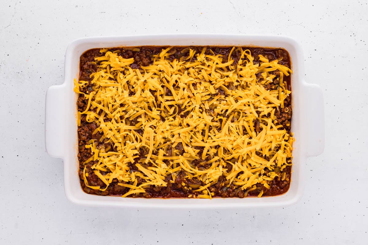 Shredded cheese added on of the sloppy joe mixture in a baking dish.