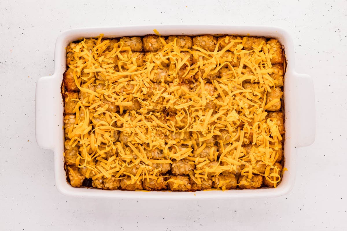 Shredded cheese added on top of the layer of tater tots in a baking dish.
