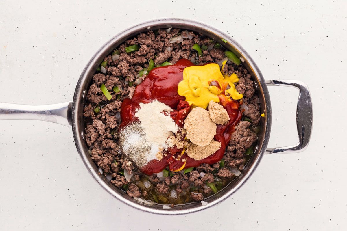 Overhead shot of ground beef with onions and bell peppers, with sauces, sugar, and spices added.