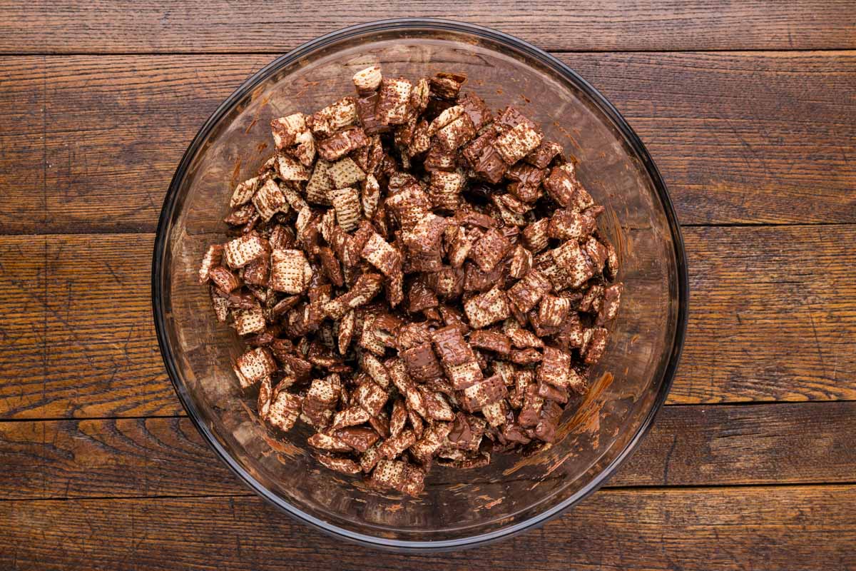 Melted chocolate folded into chex cereal in a bowl.