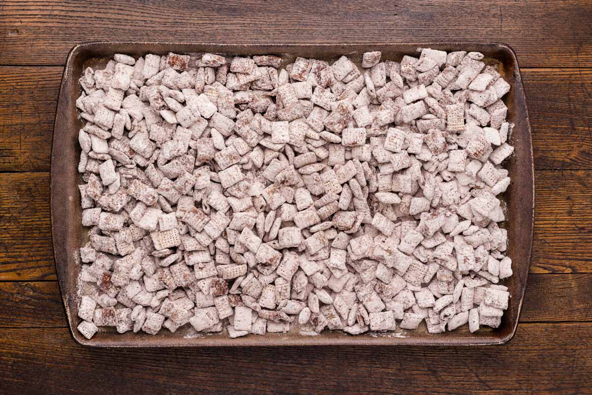 Rice chex mixed with chocolate and powdered sugar placed onto a sheet pan.