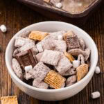 Bowl of s'mores muddy buddies with dried marshmallows and pieces of chocolate mixed in.