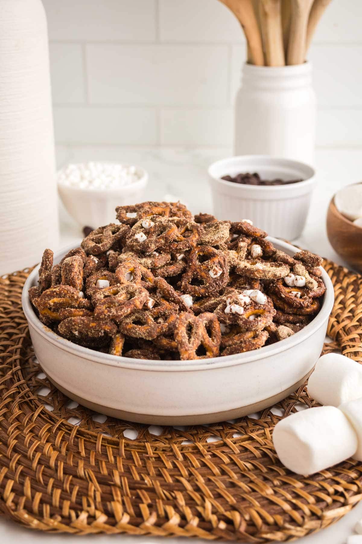S'mores pretzel snack mix served in a bowl next to some marshmallows.