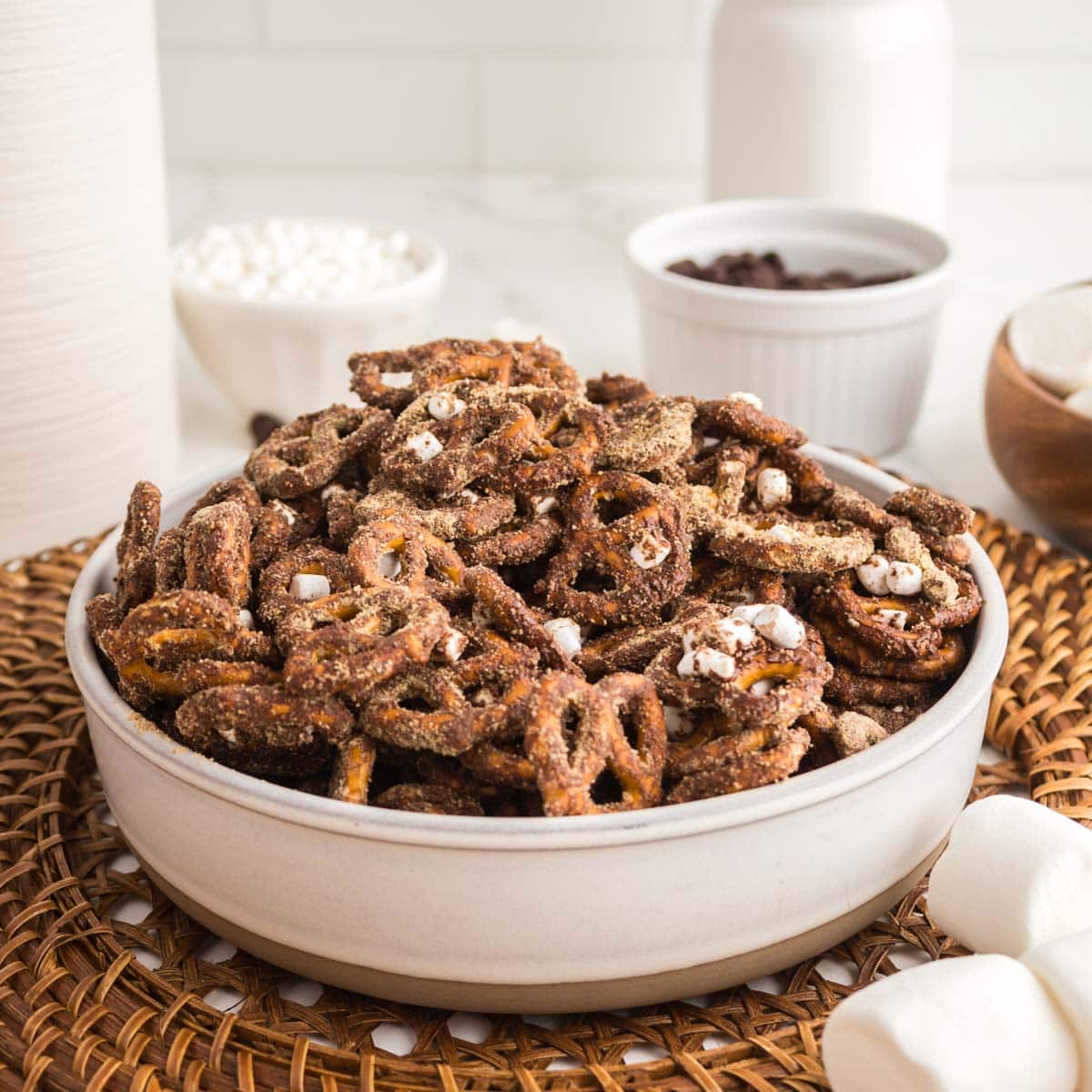 Heaping bowl of s'mores pretzels next to marshmallows.