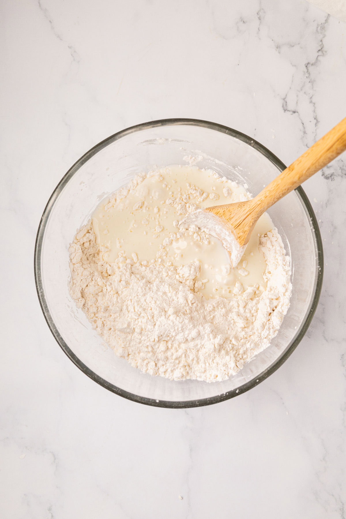 Stirring buttermilk into flour with a wooden spoon.
