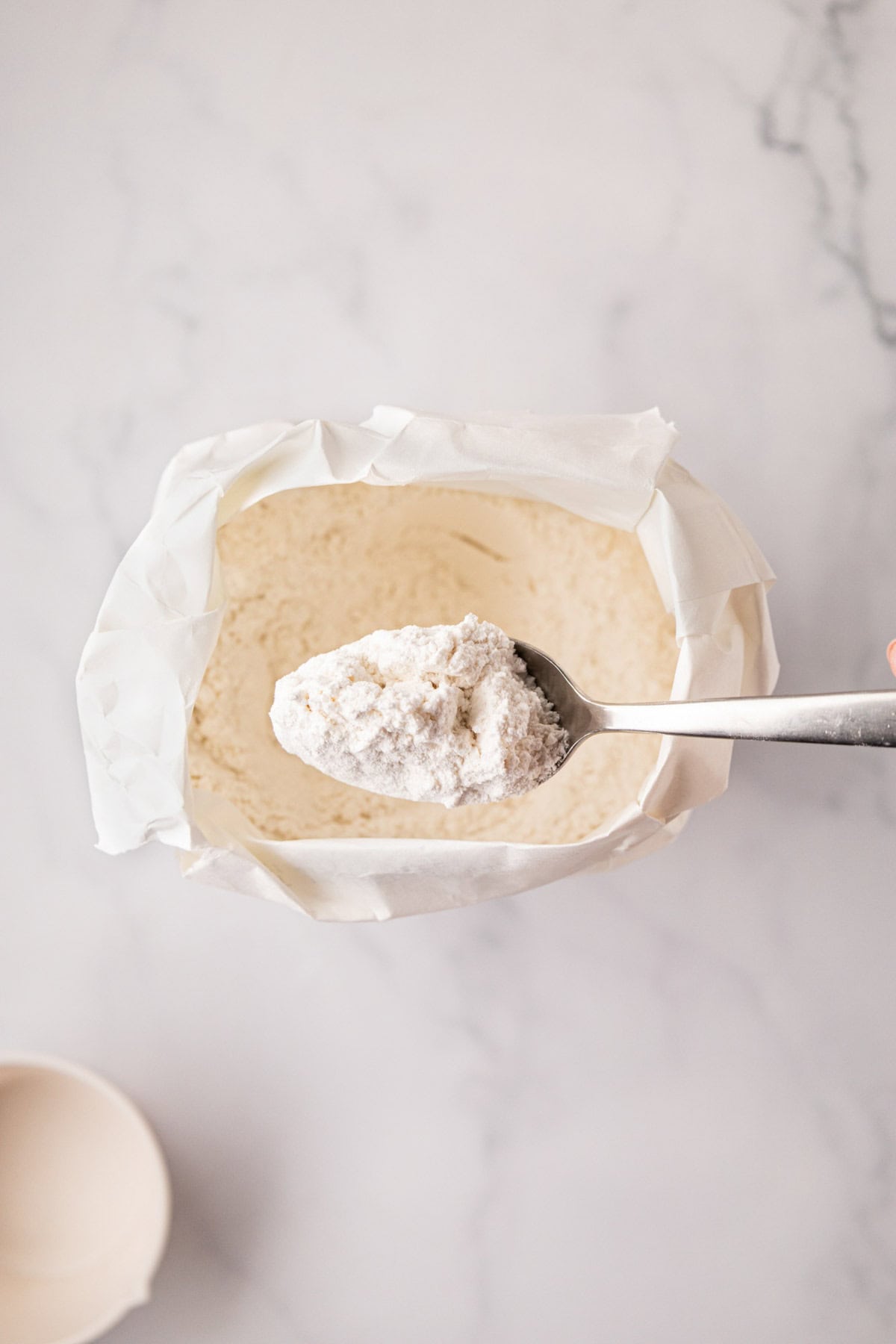 A spoon scoop fluffed up flour out of a white lily flour bag.
