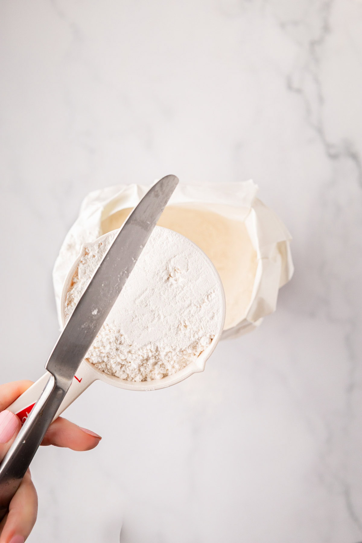 Using a knife to level off flour in a measuring cup.