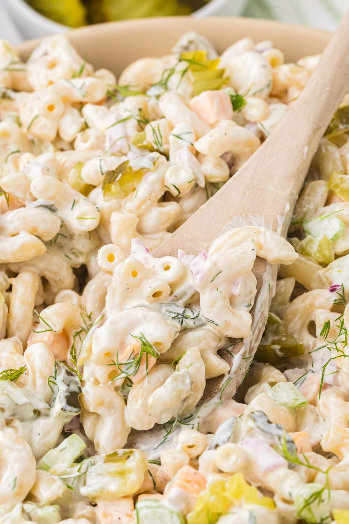 Close up of a wooden spoon in a big bowl of dill pickle pasta salad.