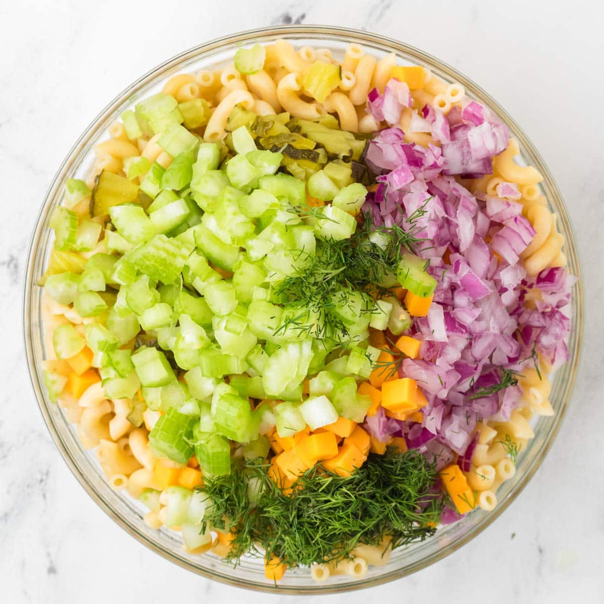 Cooked pasta topped with chopped dill pickles, red onion, celery, cheese cubes, and dill.