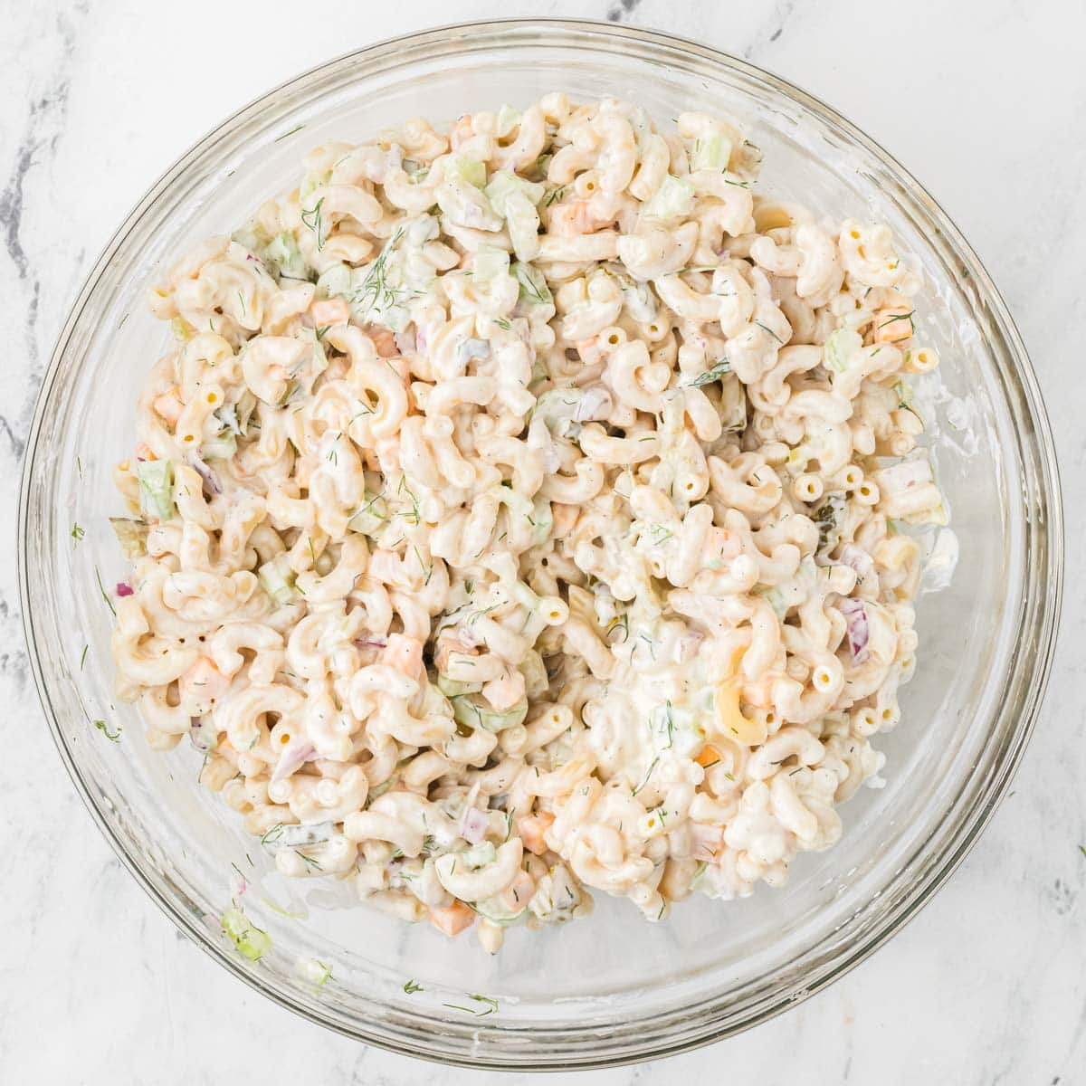 Dill pickle pasta salad all mixed together with the dressing in a large bowl.