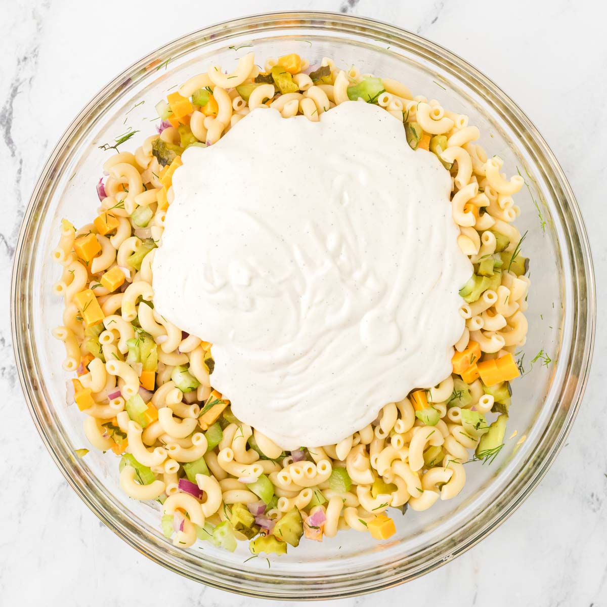Dill pickle dressing poured on top of dill pickle pasta salad before being mixed.