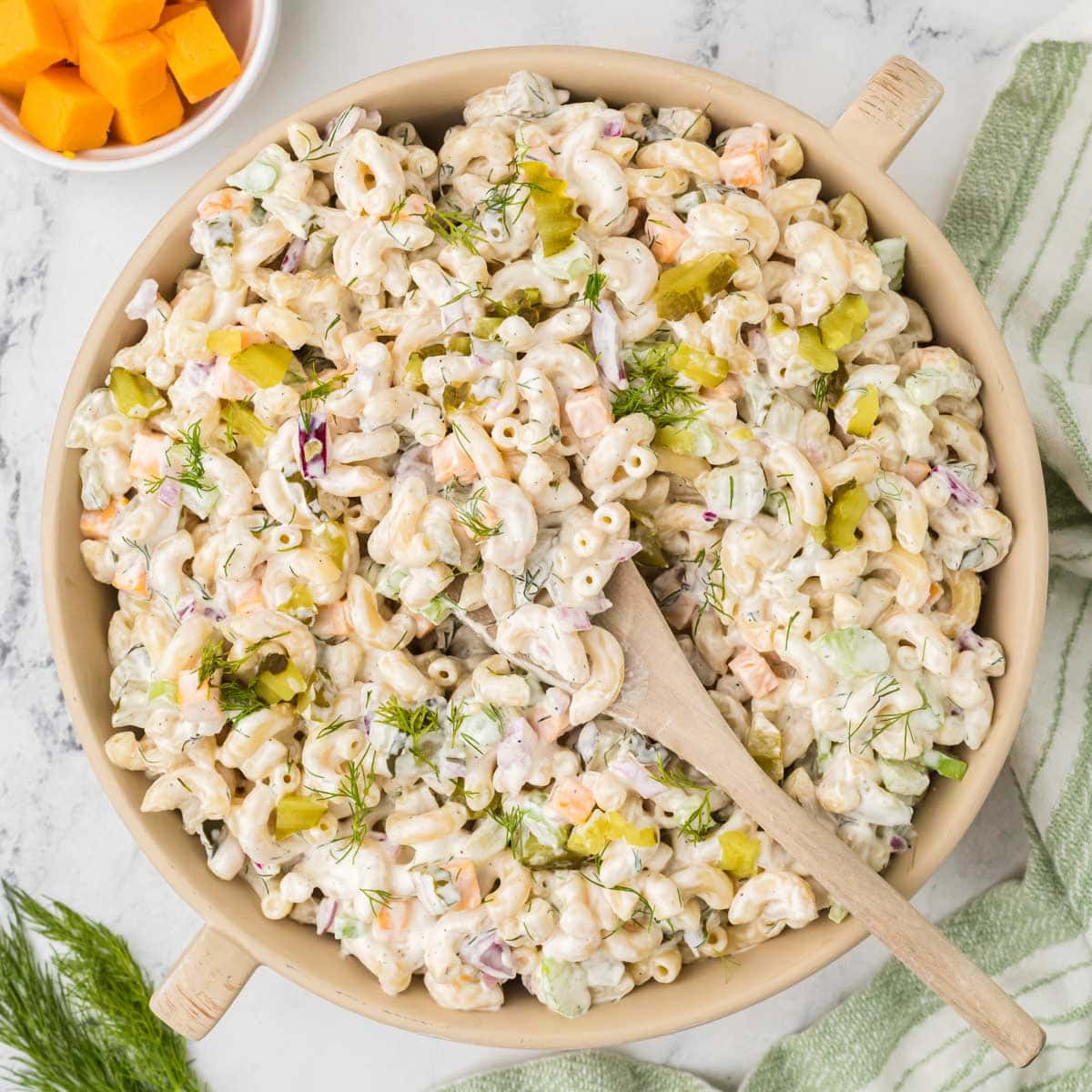 Overhead shot of dill pickle pasta salad in a large bowl with a wooden spoon.