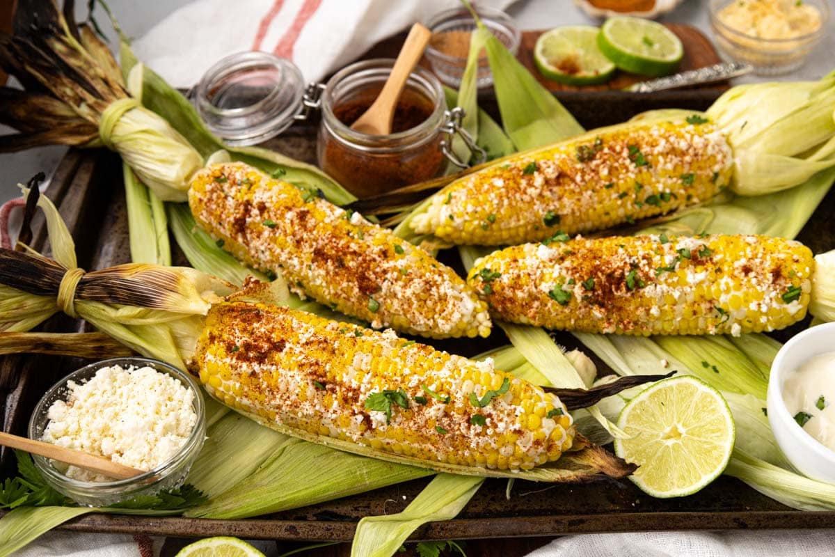 Grilled elote on a tray with all the toppings.