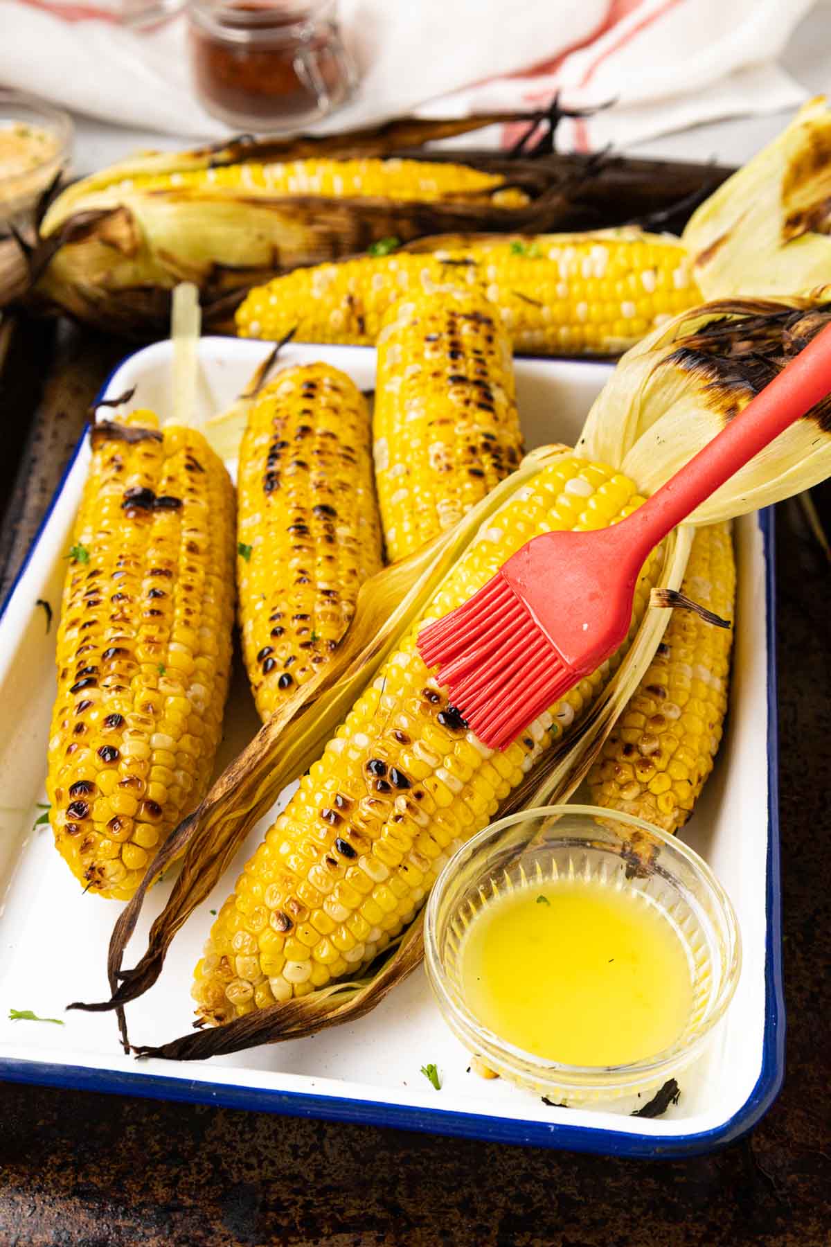 Brushing grilled corn with melted butter.