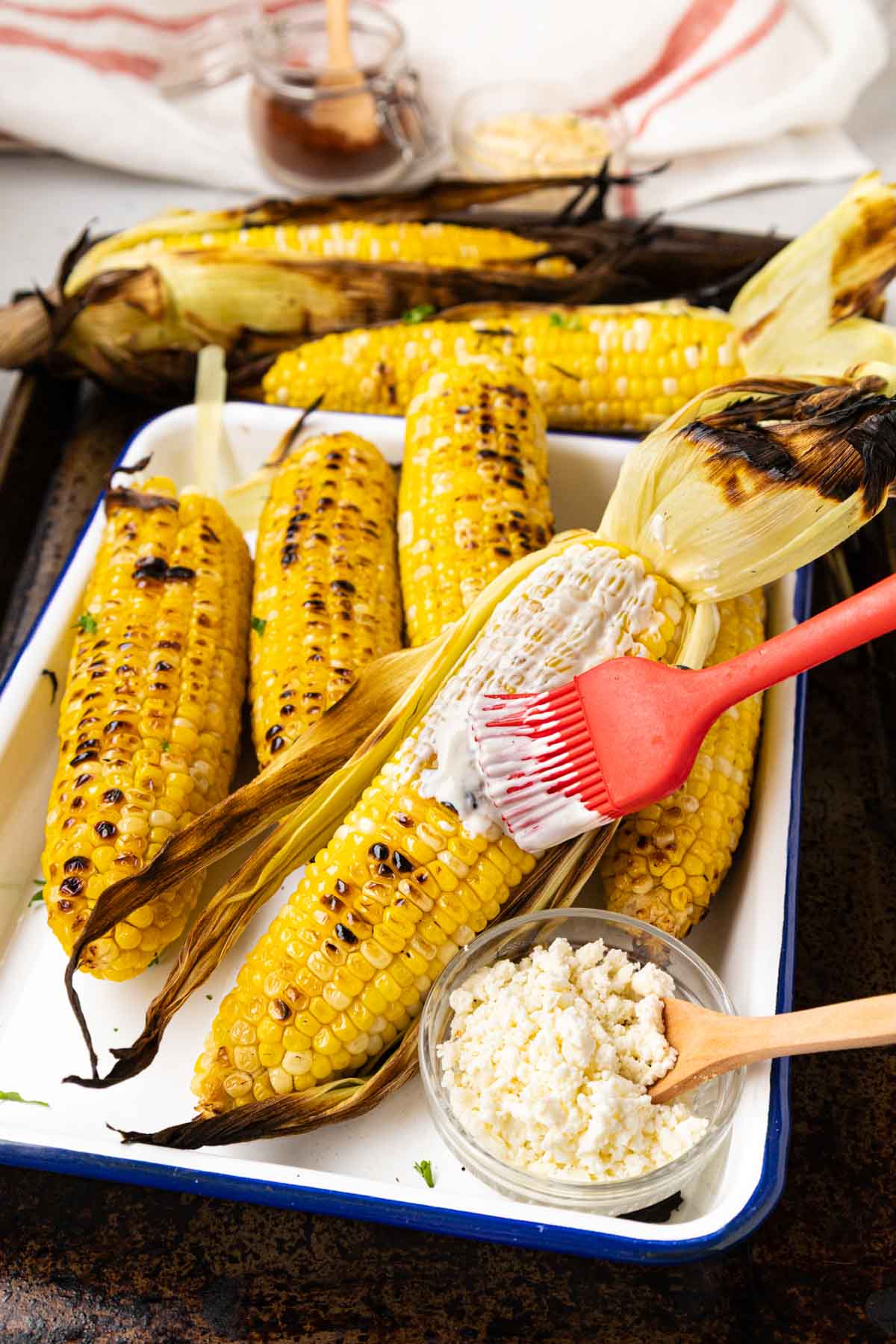 Brushing the grilled corn with the mayo, sour cream and lime juice mixture.