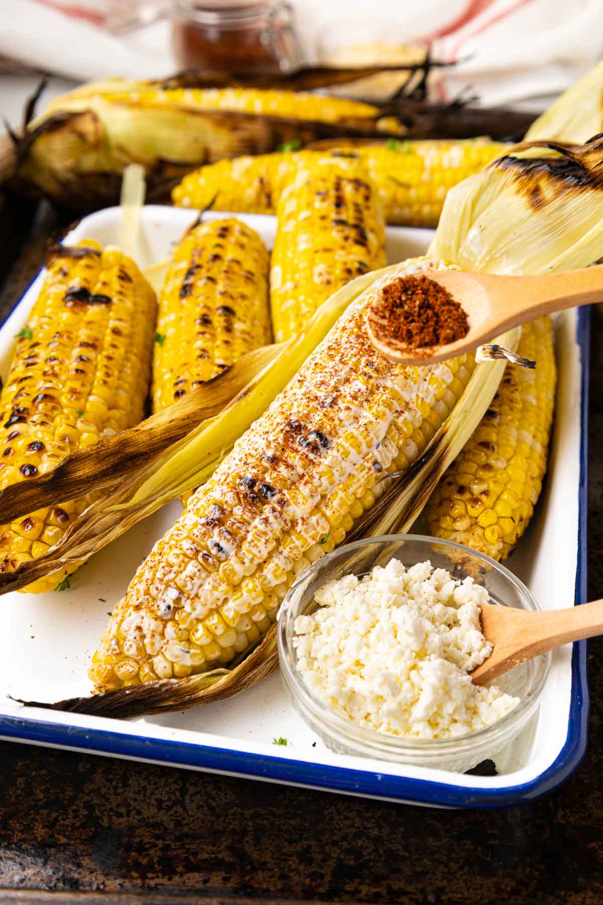Sprinkling Elote seasoning over the mayo mixture on elote.