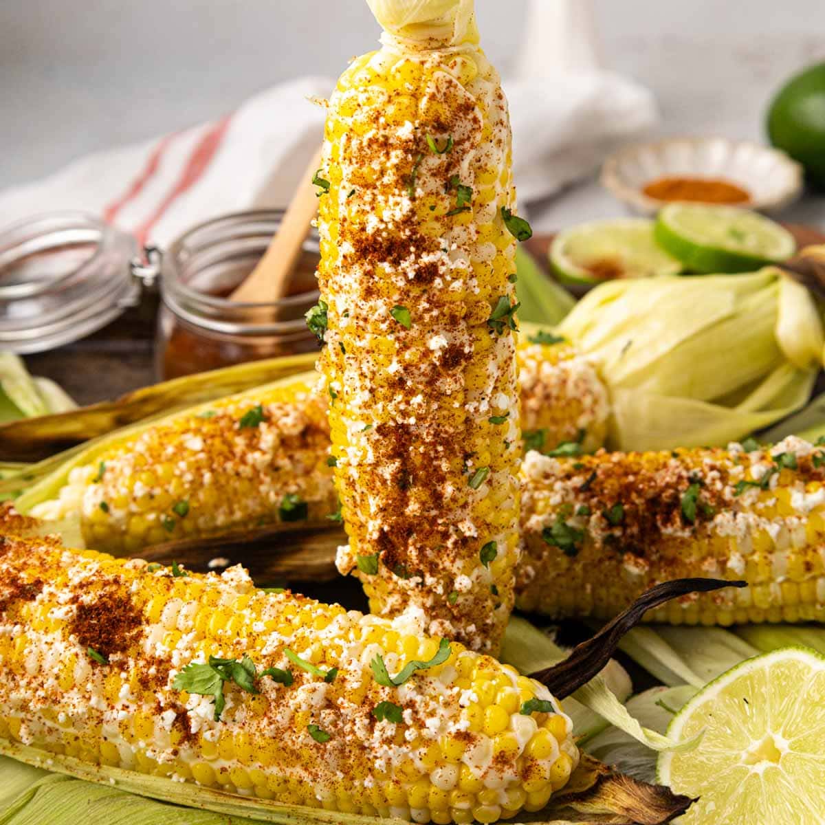 Holding a piece of Mexican street corn upright over a wooden tray of corn.