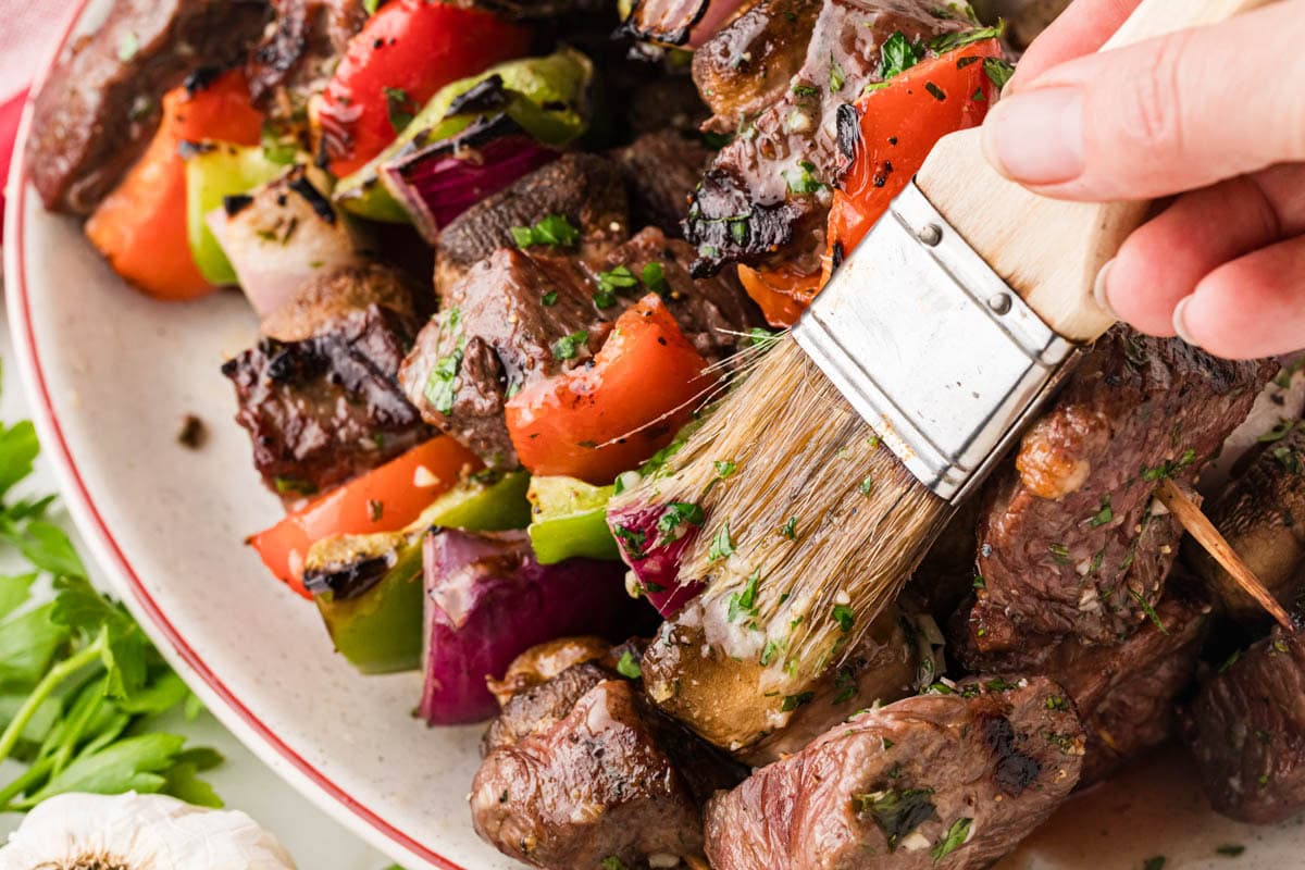 Brushing reserved garlic butter on the cooked steak kabobs.
