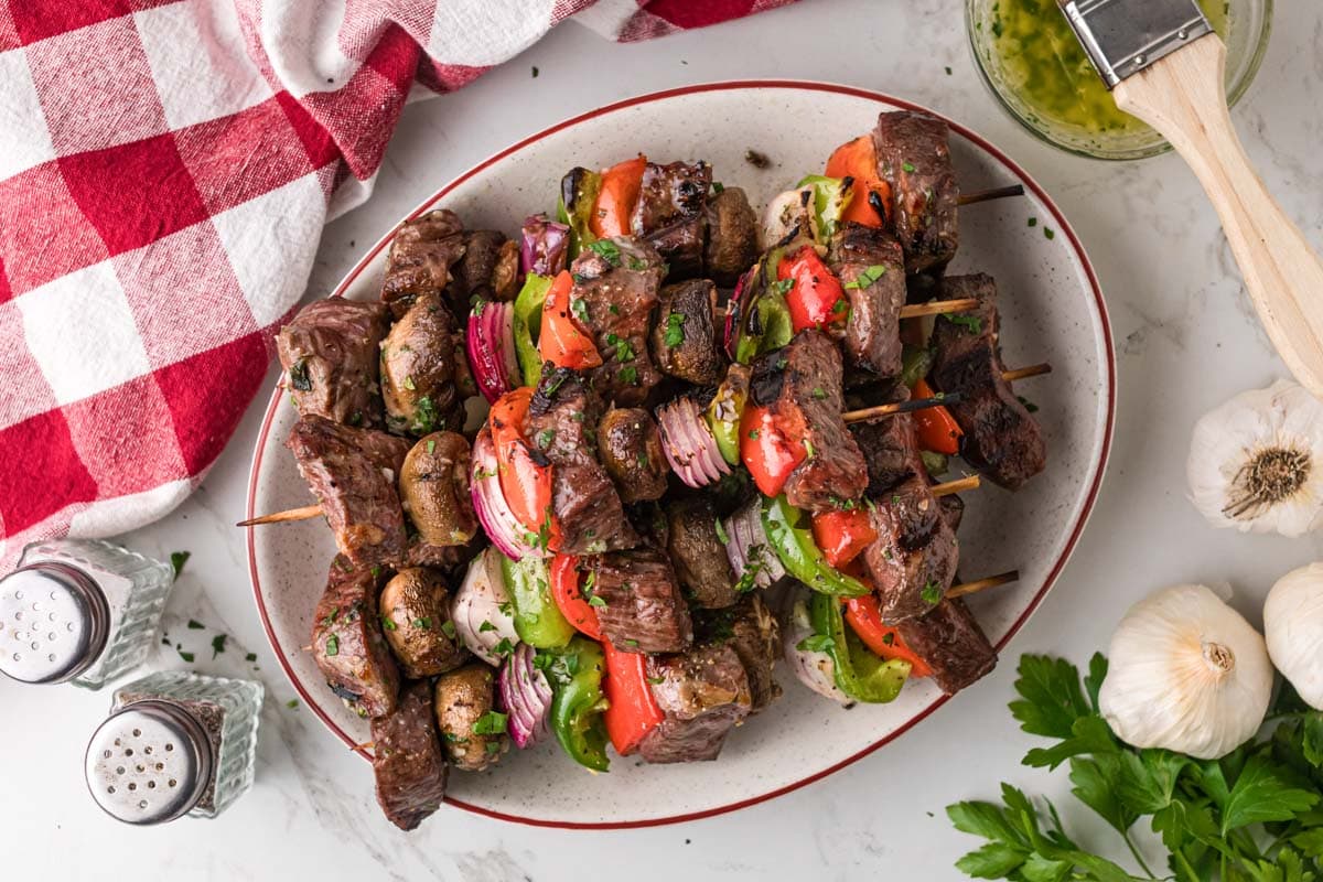 A white serving plate full a skewers with grilled steak kabobs.
