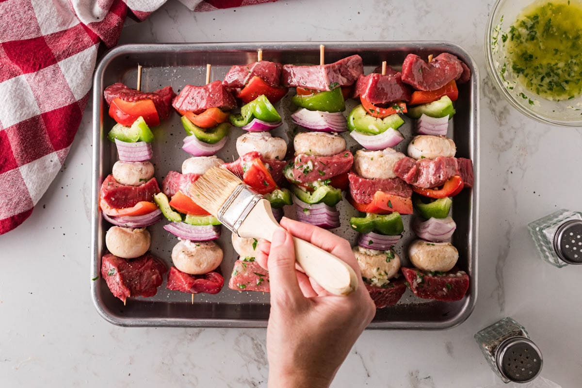 Brushing garlic butter marinade on steak kabobs.