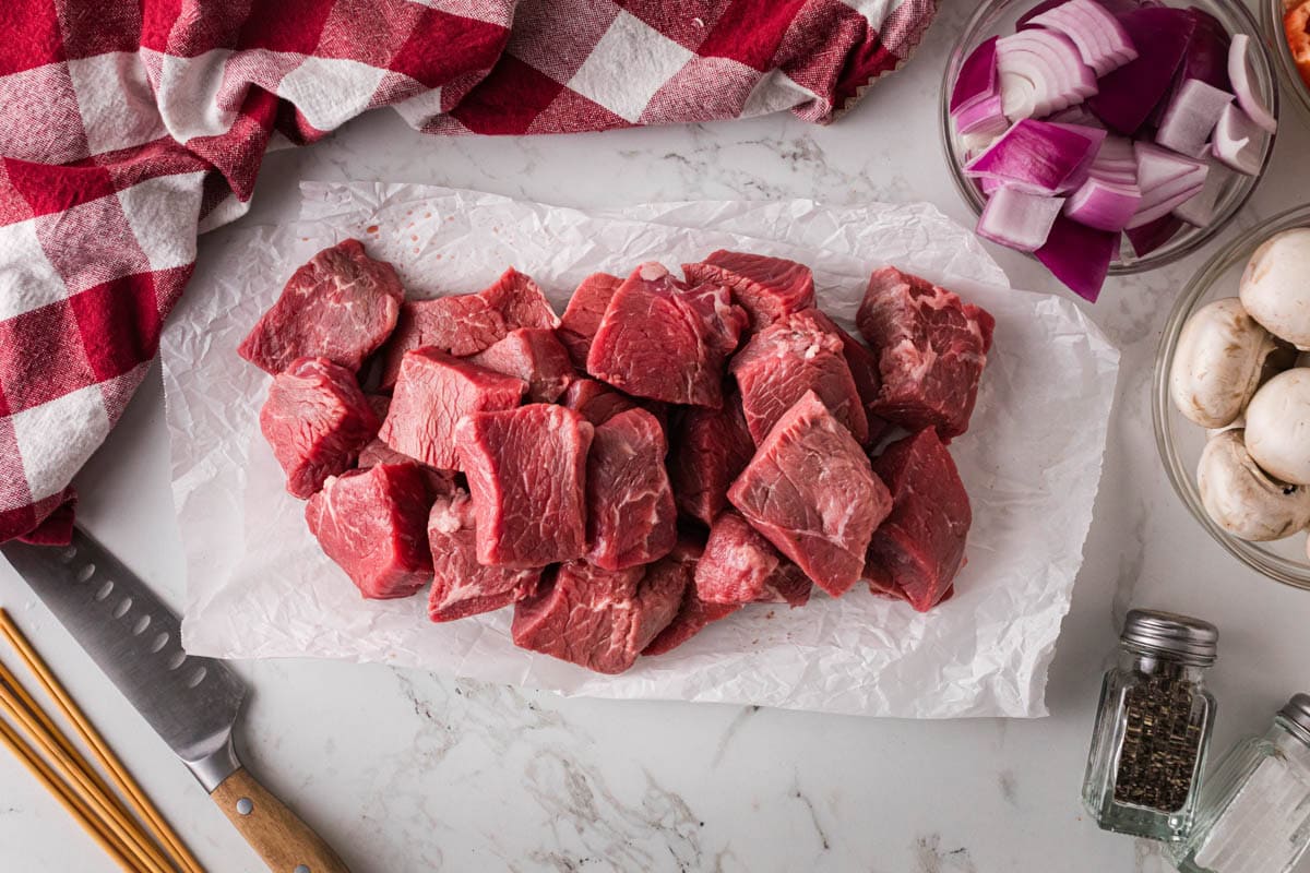 Steak cut into cubes on parchment paper.