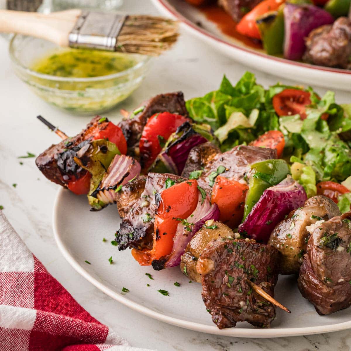 Garlic Butter steak shish kabobs with peppers, onions and mushrooms on a plate with salad.