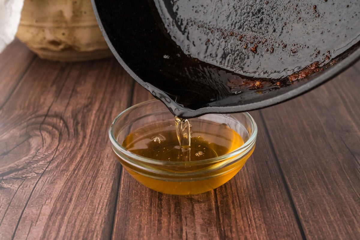 Pouring bacon grease from the cast iron skillet to a bowl.