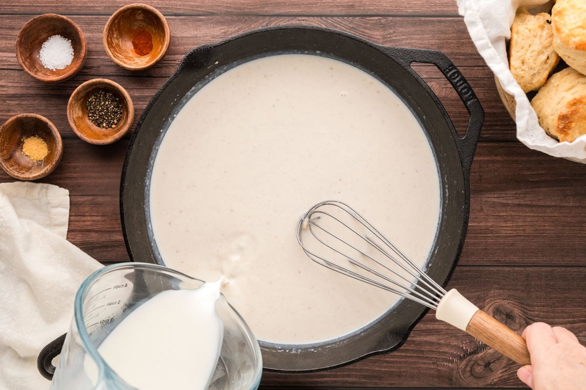 Whisking milk into the roux to make gravy base.