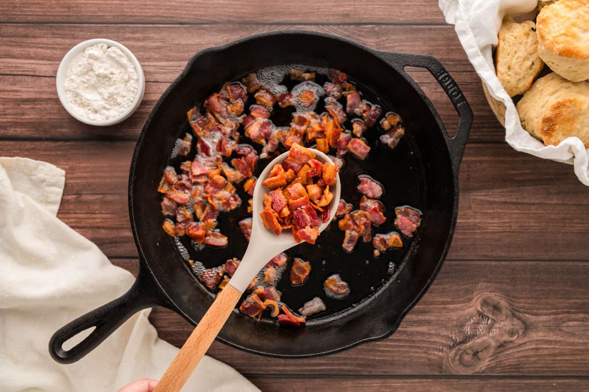 Removing cooked bacon pieces from a cast iron skillet.