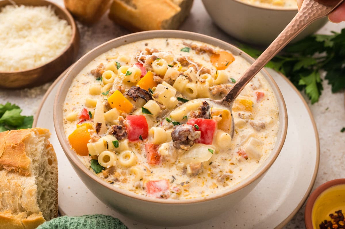 Bowl of creamy Italian sausage soup with a spoon picking a bite up.