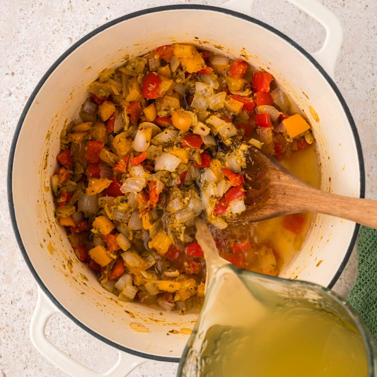 Broth being poured into a Dutch oven with onions and peppers.