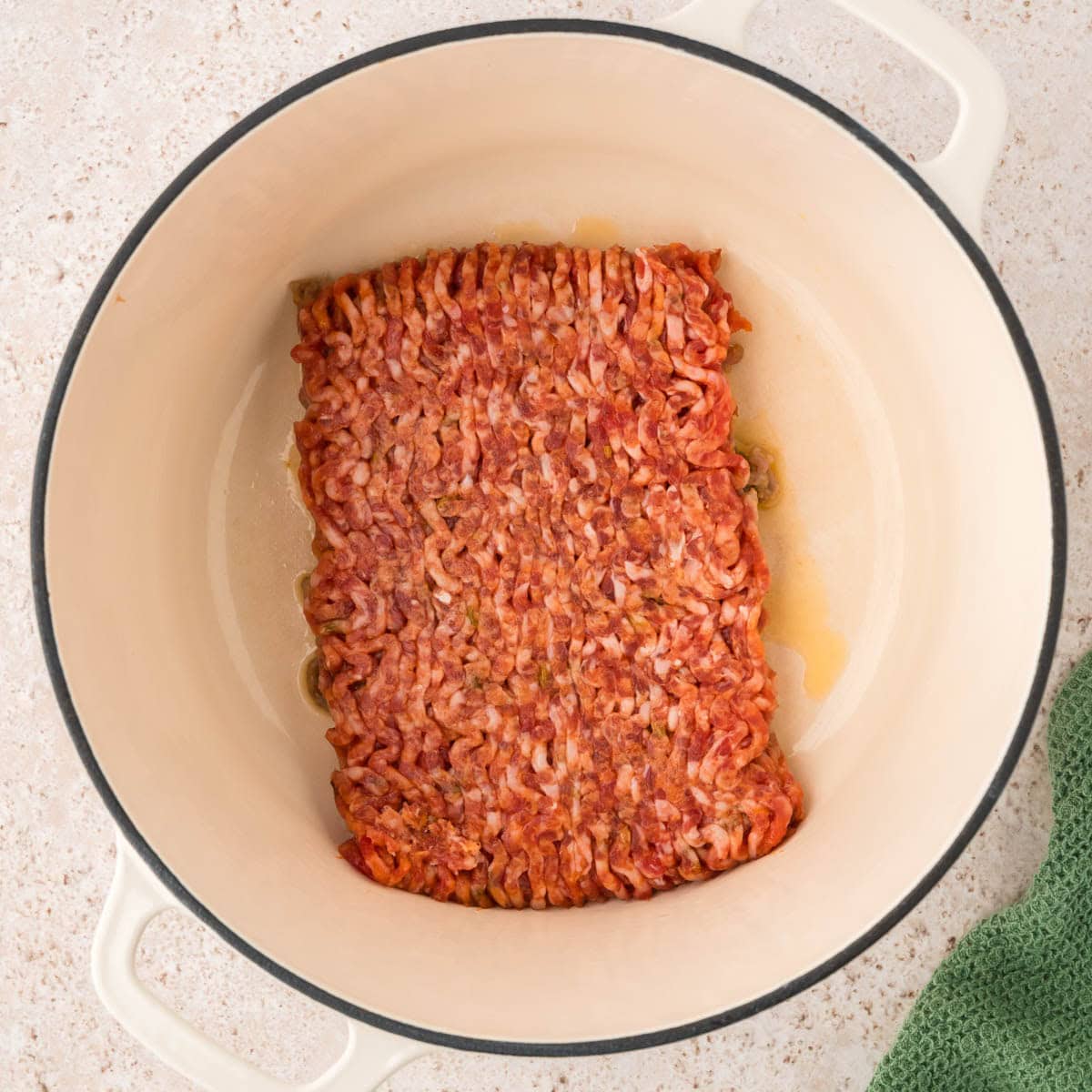 Raw ground sausage placed in a large Dutch oven to cook.