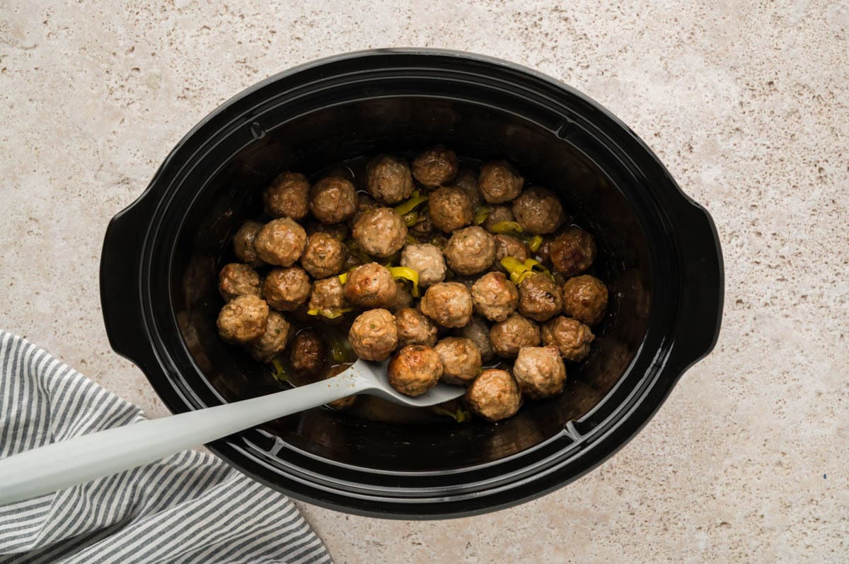 Stirring the finished Mississippi meatballs in a slow cooker.