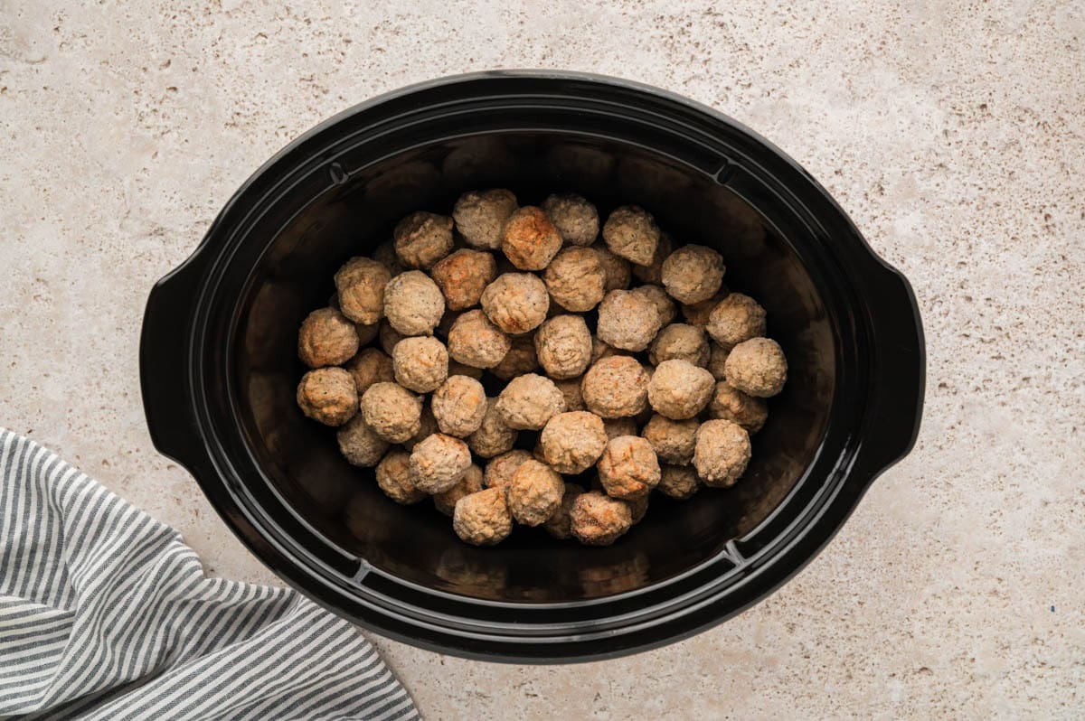 Frozen meatballs placed in the bottom of a crockpot.