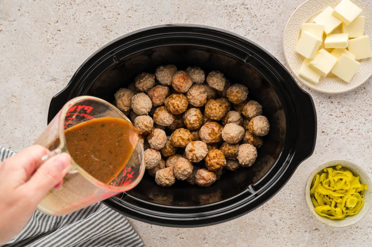 Pouring the gravy liquid mixture over the meatballs in a slow cooker.