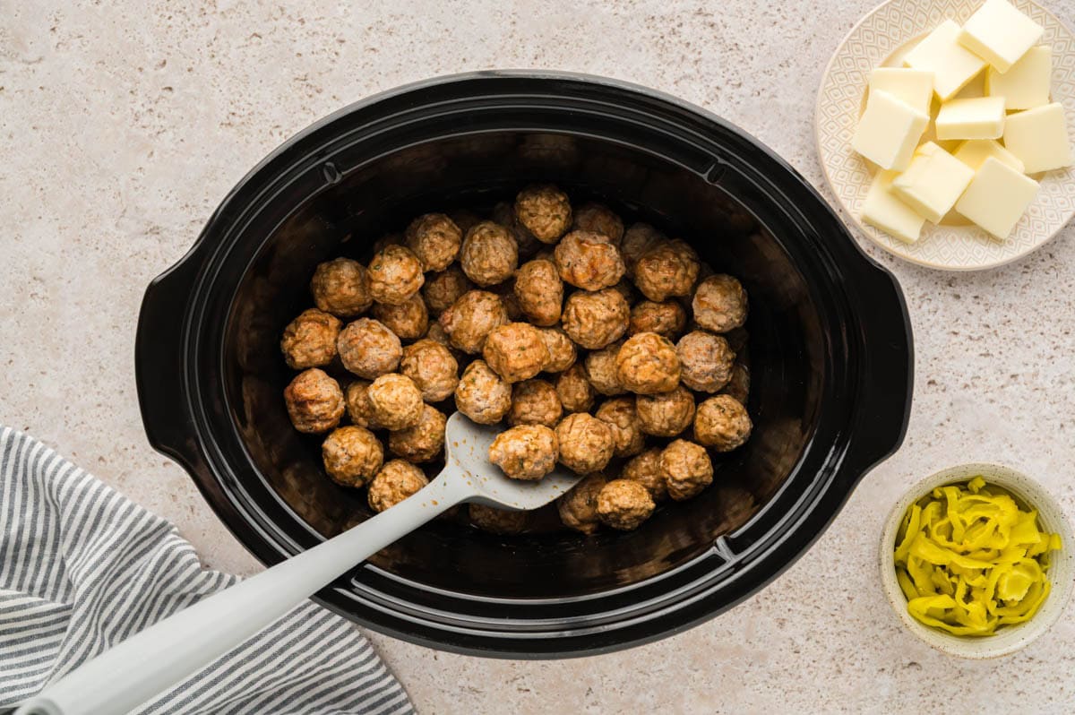 Stirring the frozen meatballs in the gravy mixture in a slow cooker.