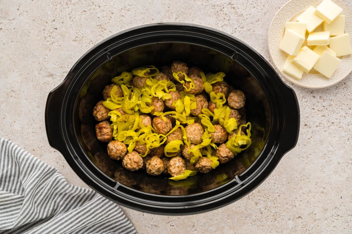 Pepperoncini peppers placed on top of meatballs in a crockpot.