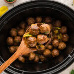 Wooden spoon scooping up some Mississippi meatballs hovering over the slow cooker.