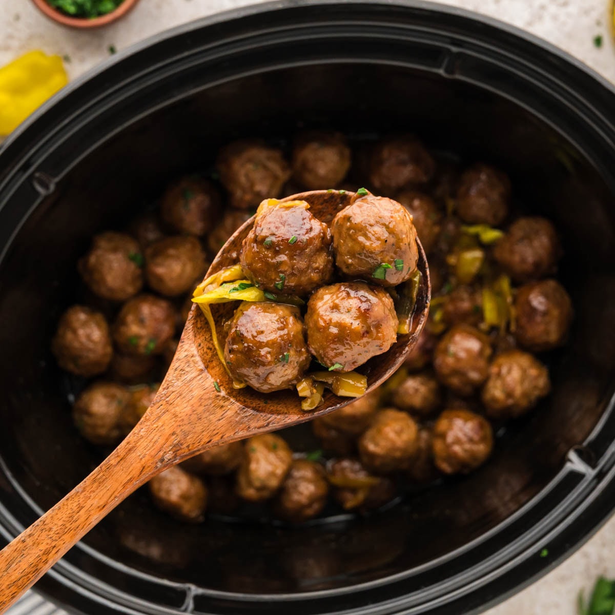 Wooden spoon scooping up some Mississippi meatballs hovering over the slow cooker.
