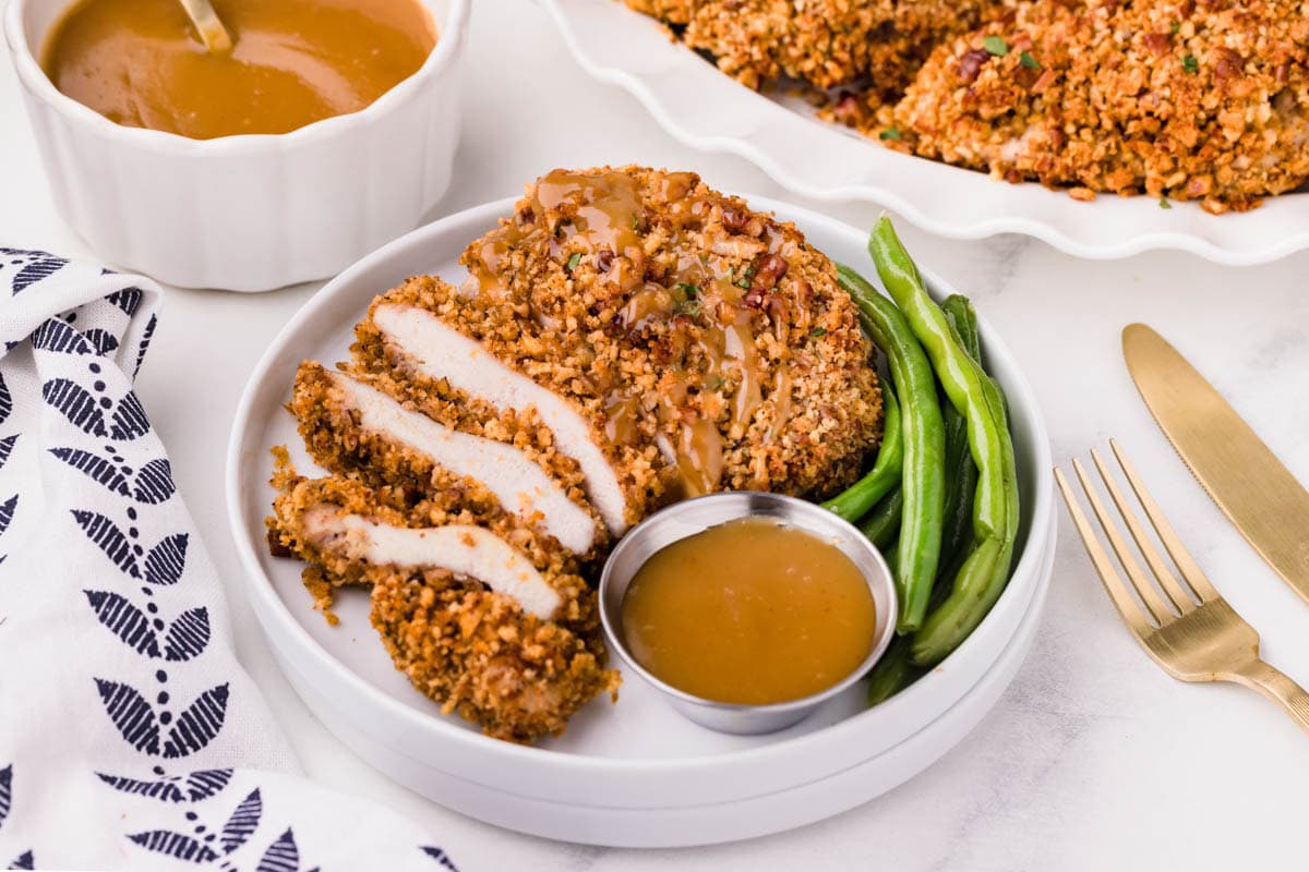 Sliced pecan crusted chicken served on a plate with a side of honey mustard sauce.