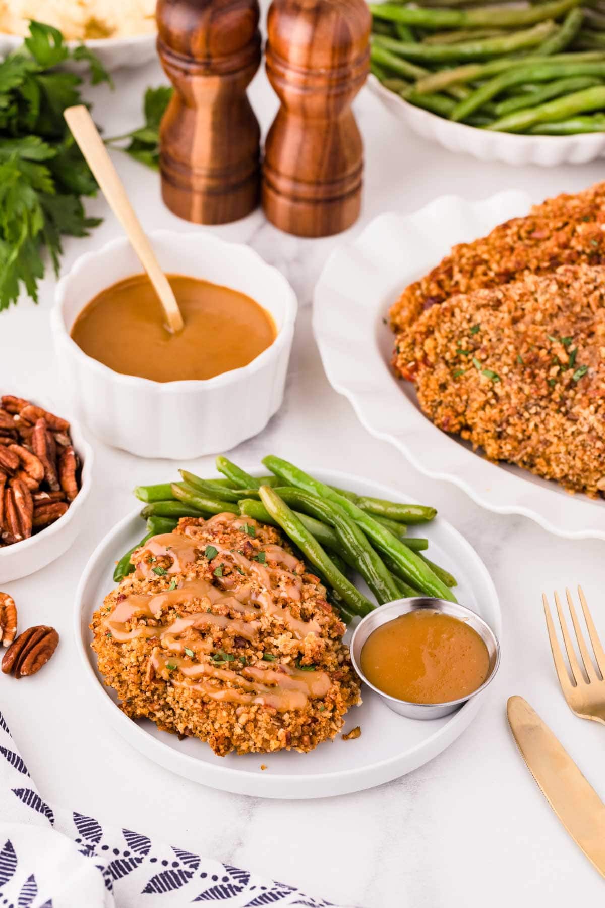 Pecan crusted chicken on a plate with green beans and sauce.