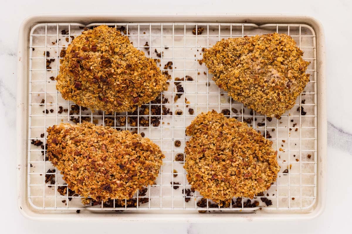 Baked pecan crusted chicken on a sheet pan lined with a wire rack.