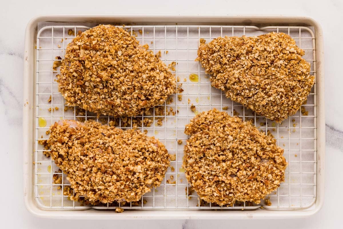 Four pecan crusted pieces of chicken on a wire rack lined sheet pan.