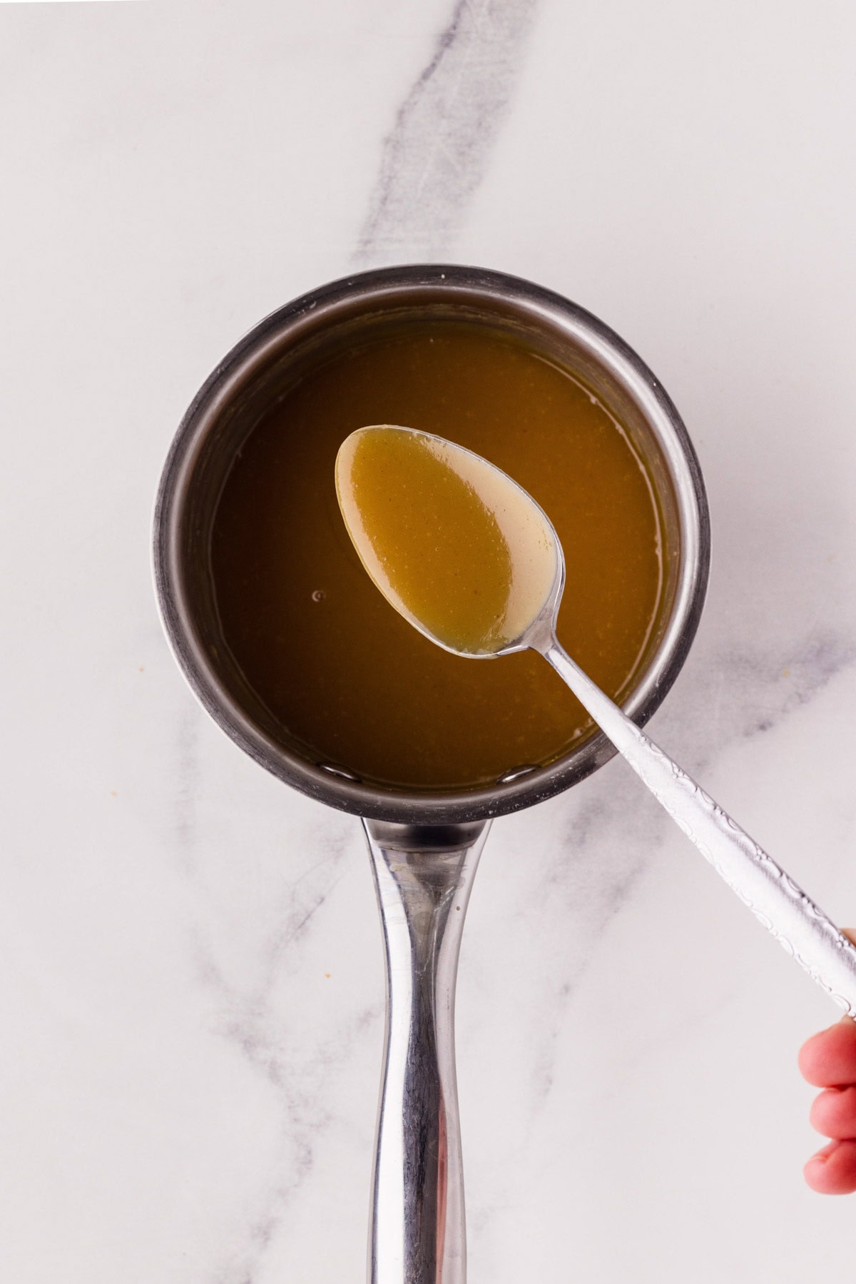 Spoon lifting up some honey mustard sauce from a saucepan.