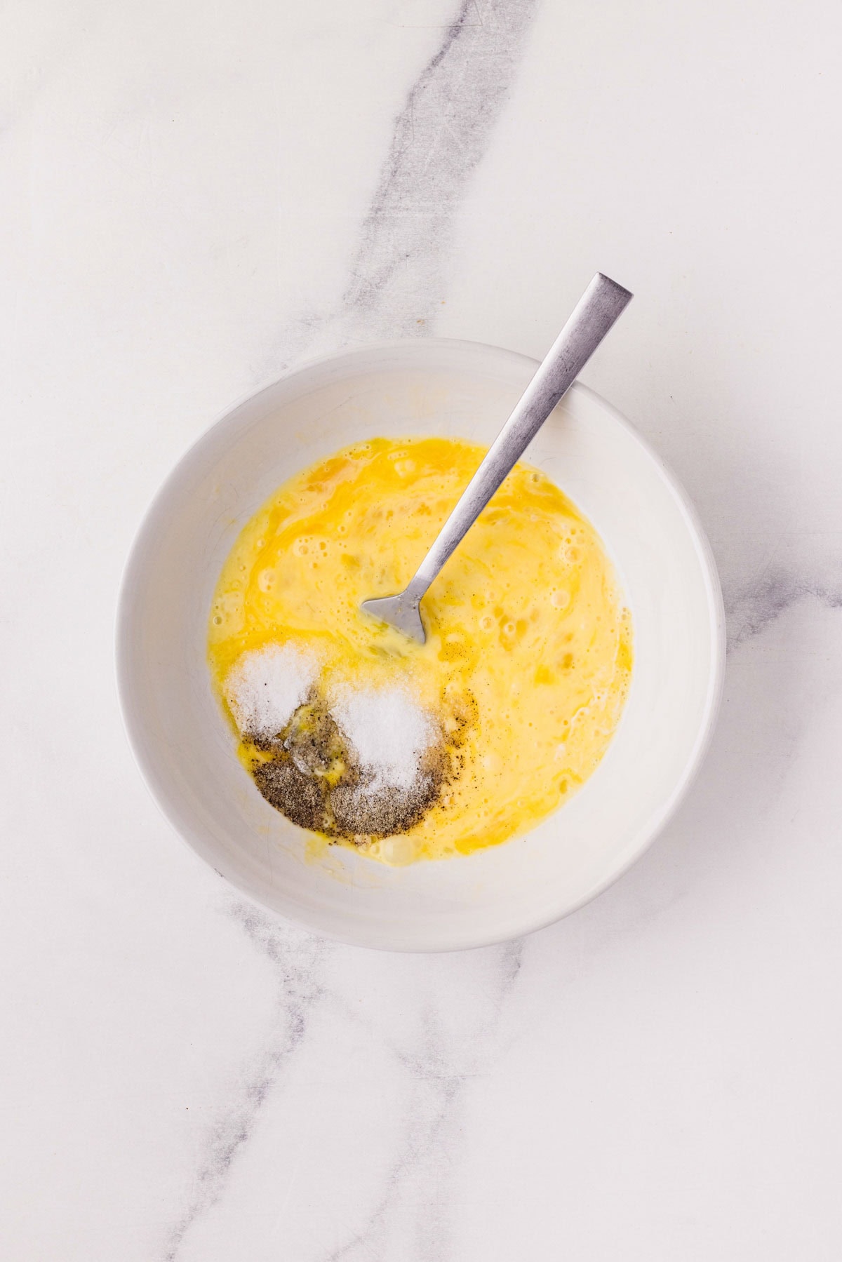 Eggs, cream, salt and pepper being mixed together in a bowl.