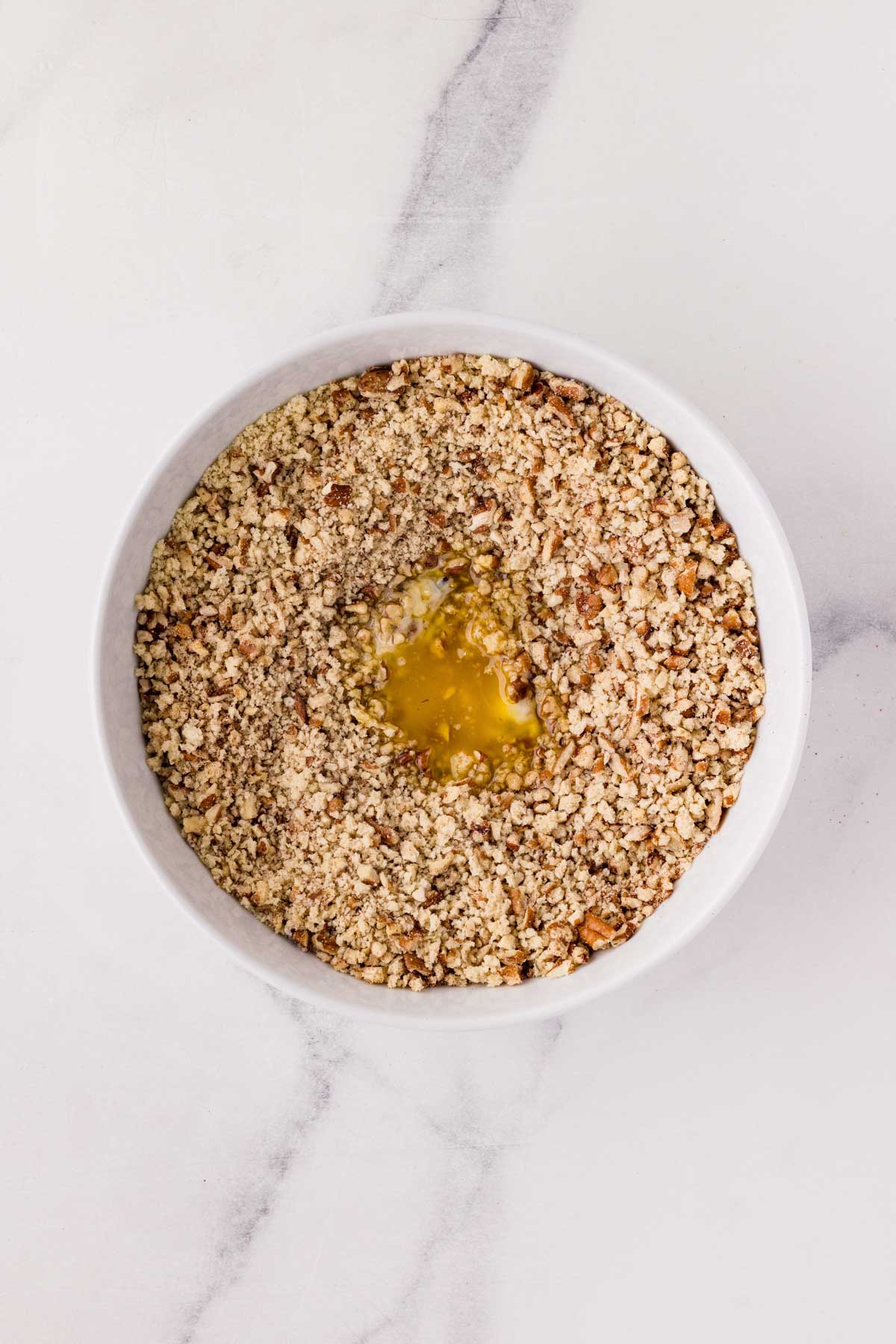 Melted butter added to the pecan breading in a bowl.