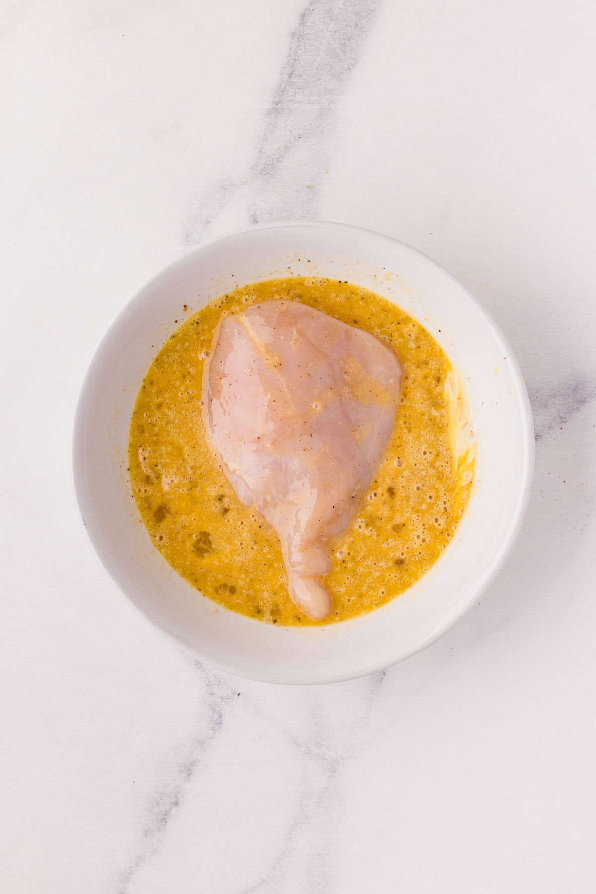 Dipping a chicken breast into the seasoned eggs in a bowl.
